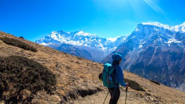 A man trekking on the Annapurna Circuit Trek, Himalayas, Nepal. Panoramic view on snow caped Annapurna chain. Lots of dried grass. High altitude, massive mountains. Freedom and adventure