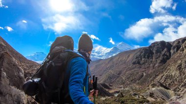Man with taking a selfie while trekking Annapurna Circus in Himalayas, Nepal, with the view on Annapurna Chain. Dry and desolated landscape. High, snow capped mountain peaks. Happiness and freedom