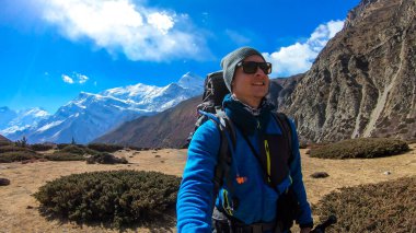 Man with taking a selfie while trekking Annapurna Circus in Himalayas, Nepal, with the view on Annapurna Chain. Dry and desolated landscape. High, snow capped mountain peaks. Happiness and freedom
