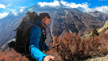 A man taking a selfie while trekking Annapurna Circus in Himalayas, Nepal, with the view on Annapurna Chain. Dry and desolated landscape. High, snow capped mountain peaks. Happiness and freedom