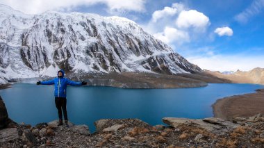 Man standing at the turquoise colored Tilicho lake in Himalayas, Manang region in Nepal. The world's highest altitude lake (4949m). Snow capped mountains around. Calm surface of the lake. Achievement