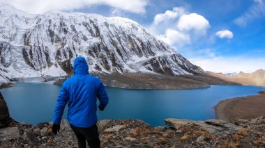 Man walking along turquoise colored Tilicho lake in Himalayas, Manang region in Nepal. The world's highest altitude lake (4949m). Snow capped mountains around. Calm surface of the lake. Achievement