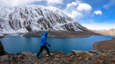 Man walking along turquoise colored Tilicho lake in Himalayas, Manang region in Nepal. The world's highest altitude lake (4949m). Snow capped mountains around. Calm surface of the lake. Achievement