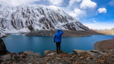 Man standing at the turquoise colored Tilicho lake in Himalayas, Manang region in Nepal. The world's highest altitude lake (4949m). Snow capped mountains around. Calm surface of the lake. Achievement