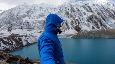 Man taking a selfie with turquoise colored Tilicho lake in Himalayas, Manang region in Nepal. The world's highest altitude lake (4949m). Snow capped mountains around. Calm surface of the lake. Freedom