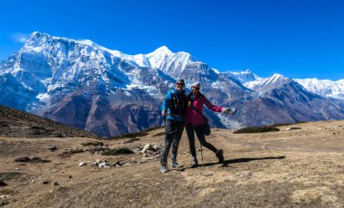 A couple hugging along the Annapurna Circuit Trek, Himalayas, Nepal. Panoramic view on snow caped Annapurna chain. Lots of dried grass. High altitude, massive mountains. Love and cheerful moments