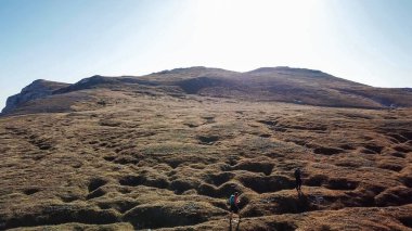 A panoramic capture of a couple hiking in Hochschwab region in Austrian Alps. The flora overgrowing slopes is turning golden. Autumn vibes in the mountains. Idyllic landscape. Freedom and wilderness