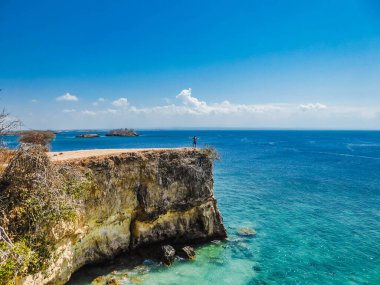 A girl standing on a dramatic cliff at the Pink Beach on the island of Lombok in Indonesia (next to Bali)