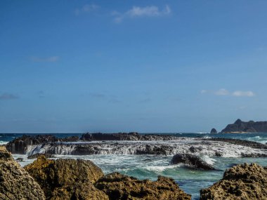 Waves splashing over dark stones in Nambung beach on the island of Lombok (next to Bali) in Indonesia.