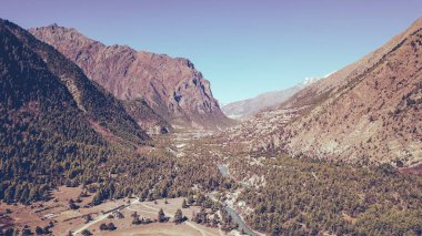 A harsh mountains slopes on the way to Upper Pisang, Annapurna Circus Trek, Himalayas, Nepal. Captured with a drone, from above. Early morning haze, in the back white mountain peaks visible.