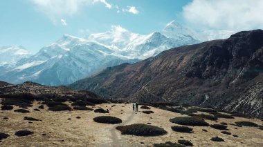 A couple trekking in the Manang Valley, Annapurna Circus Trek, Himalayas, Nepal, with the view on Annapurna Chain and Gangapurna. Dry and desolated landscape.  High mountain peaks, covered with snow.