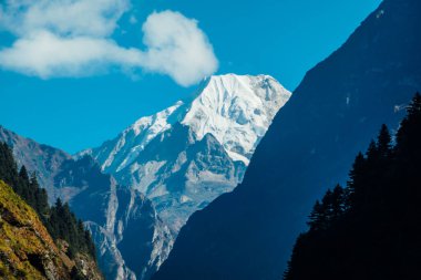 Manaslu, the eighth highest mountain in the world at 8,163 m, Annapurna Circuit Trek, Nepal. Seen from Chame. Another mountain covers the straight view on Manaslu. Light cloud over the peak.