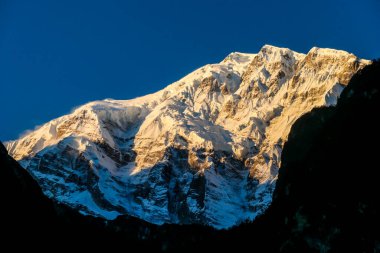 Annapurna III captured with the first sun rays on it's peak, during the sunrise. Seen from Chame, Annapurna Circuit Trek, Nepal. Clear sky above the peak. Valley still covered with shadows.