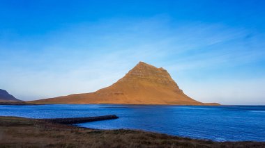 A stunning view on famous Iceland's mountain, Kirkjufell. In front of the tall hat-like mountain spreads the shallow water of a fjord. Beautiful and clear day, popular destination for a holiday.