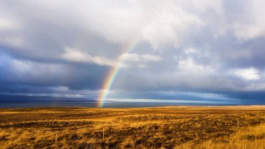 A beautiful rainbow stretching across a cloudy sky over a barren grassland. he sky looks as if it just stopped to rain. Beautiful miracle.