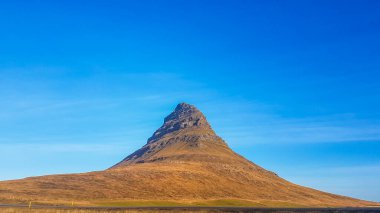 A close up on a stunning view on famous Iceland's mountain, Kirkjufell. Tall, hat-like mountain. Steep slopes of the hill. Beautiful and clear day, popular destination for a holiday.