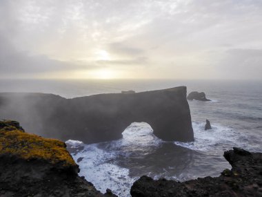 Dyrhlaey, the arch with the whole, located on the shore, in the sea. Mystical creation. Arch looks like a bridge, that does not connect anything. Waves rushing to the shore, misty atmosphere
