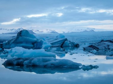 Beautiful glacier lagoon. Thousands of icebergs drifting lazily towards the sea, shining in many shades of blue. Soft sunset in the back. Thick clouds above the lagoon. Glacier's cap in the back