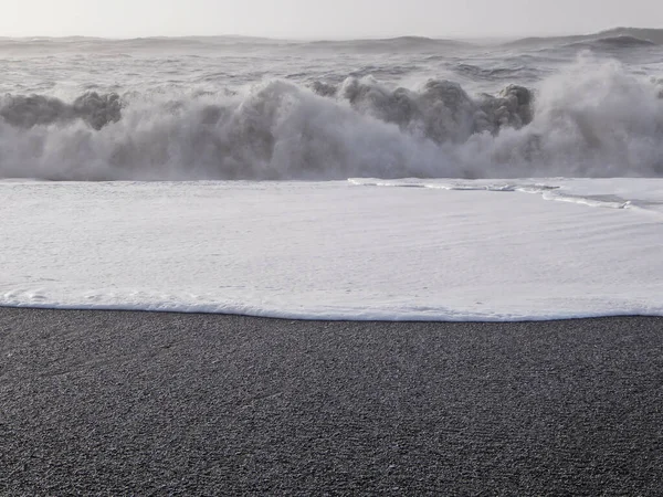 Reynisfjara is a world-famous black-sand beach found on the South Coast of Iceland. White foam contrasted with black sand. Rough sea pushes the foam far into the shore. Dangerous sea.