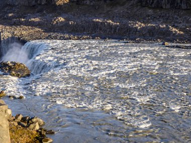 An upper part of a waterfall splashing a lot of water drops around, caught on a sunny day. Lots of sharp rocks around the waterfall. Wide bank of the river. Amazing power and beauty of nature.