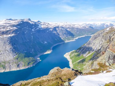 A beautiful view from the above on Ringedalsvatnet lake, Norway. Lake is located in between tall mountains. Slopes of the mountains are partially covered with snow. The water of the lake is navy blue.