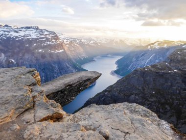 Famous rock formation, Trolltunga with a view from the above on Ringedalsvatnet lake, Norway. Rock hanging. Slopes of the mountains are partially covered with snow. Soft colors of the sunrise