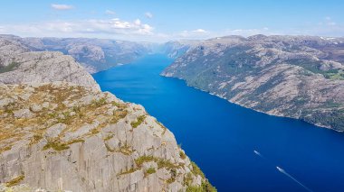 A stunning view on Lysefjorden from Preikestolen. Surface of the water located 600m below. A ship moving through it.  Steep cliffs are joining the water on both sides. A bit of mist in the back.