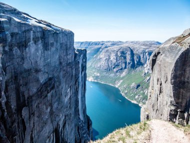 A view from the top of a mountain on stunning Lysefjorden shimmering with many shades of blue and green. Steep slopes of the mountain,waterfall rushing down the steep slopes. Harsh and barren slopes.