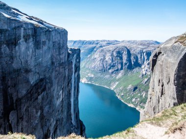 A view from the top of a mountain on stunning Lysefjorden shimmering with many shades of blue and green. Steep slopes of the mountain,waterfall rushing down the steep slopes. Harsh and barren slopes.