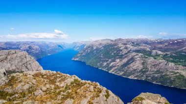 A stunning view on Lysefjorden from Preikestolen. Surface of the water located 600m below. A ship moving through it.  Steep cliffs are joining the water on both sides. A bit of mist in the back.