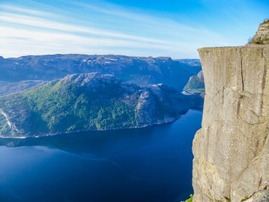 A view on Preikestolen, Pulpit Rock, Norway and Lysefjorden below it. Characteristic rock formation. Steep cliffs join the water. Barren rocks on the top. Clouds are arranged in longitudinal lines