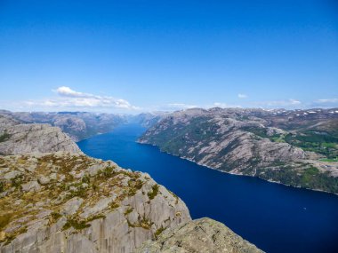 Endless view on Lysefjorden seen from Preikestolen, Norway. Steep cliffs join the water. Few ships on the water. Clear and bright day. Barren rocks on the top of the cliffs, partially snow-capped