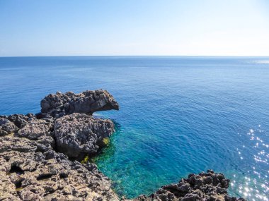 Kıbrıs, Cape Greco 'da mavi bir göl. Suyun birçok mavi tonu vardır. Kristal berrak su. Denizden çıkan keskin kayalar. Denizin sakin yüzeyi. Parlak ve güneşli bir gün.