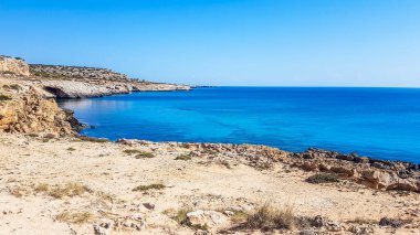 A stony shore of a Cape Greco in Cyprus. Salty water shapes the stone. Sharp and dangerous rocks. Cliffs meeting the sea wter. Barren slopes. sea line blends with the horizon line. Paradise beach.