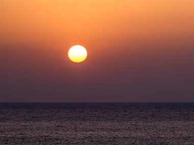 A stunning sunset over the sea. Sun sets directly into the water. Sky is dark orange and the water has a darker shade. Night wins over the day. Paphos, Cyprus.