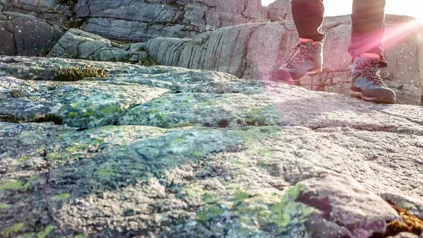 A close up on a male hiking boots. The man is walking front. Soft sunrise beams are lighting the way. Rocks overgrown with moss. Barren and empty landscape.