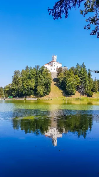 A view on Trakoscan castle from the lake side. Castle is located on a small hill and well hidden in between the trees. The lake in front of the castle is really green. Clear and bright day.