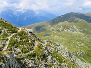 Hiking trail in the high mountain. Lush green grass covers the slopes. Endless chains of mountains visible. . Lots of sharp rocks next to the trail. Spring in the mountains.A little overcast.