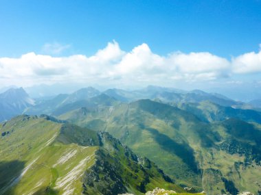 A stunning view on Alpine valley. Hiking trails in the high mountain. Green grass and bushes cover the slopes. Endless chains of mountains visible. Partially cloudy day. Spring in the mountains.