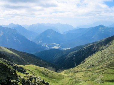 A stunning view on Alpine valley. Hiking trails in the high mountain. Green grass and bushes cover the slopes. Endless chains of mountains visible. Thick clouds on the sky. Spring in the mountains.
