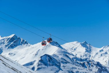 Two gondolas going up and down above the snow caped mountains. Gondolas are moving on thick ropes hanging very high. In the back there are tall Alps. Ski resort in Heiligenblut, Austria.