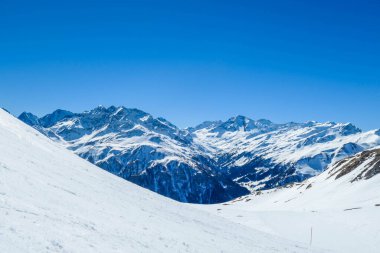 A beautiful and serene landscape of mountains covered with snow. Thick snow covers the slopes. Clear weather. Sharp slopes of the mountains covered with snow, with partially visible rocks.
