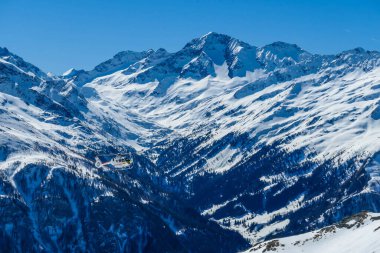 A rescue helicopter in the high mountains. Tall Alps surrounding the vehicle that is getting ready to land. Mountains slopes are covered with thick snow. Dangerous rescue mission.