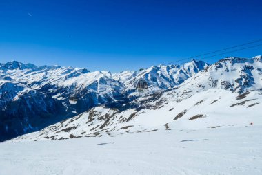 Two gondolas going up and down above the snow caped mountains. Gondolas are moving on thick ropes hanging very high. In the back there are tall Alps. Ski resort in Heiligenblut, Austria.