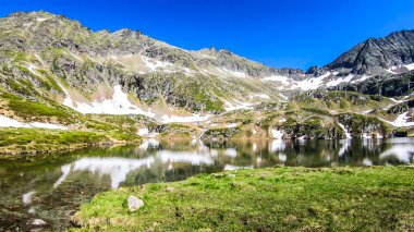 View on an icy-cold alpine lake. There is a lot of snow around on mountain's slopes. Spring is slowly coming into the valley. Calm surface of the lake reflects the mountains. Schladming Alps, Austria