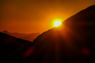 Sun setting behind a massive mountain range of Schladming Alps, Austria. The slopes are steep, partially covered with snow. Dangerous mountain climbing.Clear and beautiful view. Endless mountain range