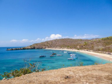 A view on a bay on Pink Beach, Lombok Indonesia. Plenty colourful boats anchored to the shore. The water has many shades of blue. The heavenly beach is surrounded by small hills. Paradise beach.