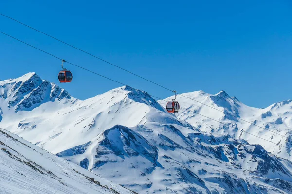 Two gondolas going up and down above the snow caped mountains. Gondolas are moving on thick ropes hanging very high. In the back there are tall Alps. Ski resort in Heiligenblut, Austria.