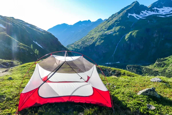An unfolded tent on a meadow in high Alps. Slopes of the mountains partially covered with snow. Wild camping in Austria. High mountains around. Spring in alpine valleys.