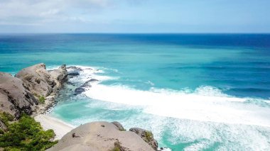 Dalgalar Tanjung Aan sahilinin keskin uçurumlarına vuruyor. Cennetin sahilinde tehlikeli bir fenomen. Su, ezici dalgaların gücünden köpürüyor. Doğanın güzelliği.